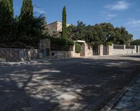 an open road and building are behind a stone fence with ivys on the front