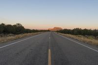 a long empty road with mountains in the distance with a car in the foreground