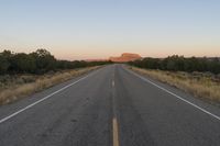 a long empty road with mountains in the distance with a car in the foreground