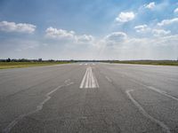 an open runway with markings in the pavement and clouds in the background, as seen from below