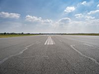 an open runway with markings in the pavement and clouds in the background, as seen from below