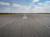 an open runway with markings in the pavement and clouds in the background, as seen from below