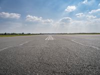 an open runway with markings in the pavement and clouds in the background, as seen from below