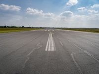 an open runway with markings in the pavement and clouds in the background, as seen from below