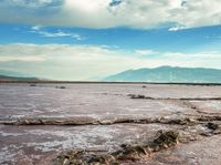 there are dead tree trunk in the water with mountains in the background behind it and clouds above