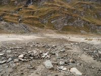 there is a sandy beach with rocks and rocks in the foreground and a large mountain covered in low cloud