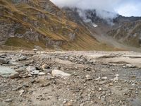 there is a sandy beach with rocks and rocks in the foreground and a large mountain covered in low cloud