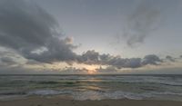 a photo taken of a beach during sunset with some clouds in the sky and water with waves lapping towards it