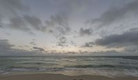 a photo taken of a beach during sunset with some clouds in the sky and water with waves lapping towards it