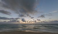 a photo taken of a beach during sunset with some clouds in the sky and water with waves lapping towards it