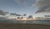 a photo taken of a beach during sunset with some clouds in the sky and water with waves lapping towards it