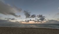 a photo taken of a beach during sunset with some clouds in the sky and water with waves lapping towards it