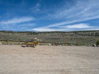 an orange dump truck parked in a gravel lot with hills and blue skies behind it