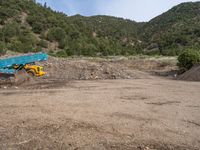 two yellow bulldozers work on sand and gravel in a mountain valley while another one looks at it