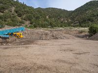 two yellow bulldozers work on sand and gravel in a mountain valley while another one looks at it