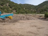 two yellow bulldozers work on sand and gravel in a mountain valley while another one looks at it