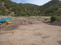 two yellow bulldozers work on sand and gravel in a mountain valley while another one looks at it