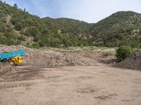 two yellow bulldozers work on sand and gravel in a mountain valley while another one looks at it