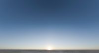 an asphalt parking lot in the middle of a desert with mountains in the background and a sun in the sky