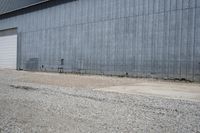 two cars parked in front of a large warehouse building with concrete wall and large door