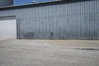 two cars parked in front of a large warehouse building with concrete wall and large door