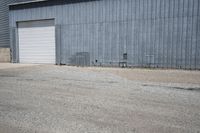 two cars parked in front of a large warehouse building with concrete wall and large door