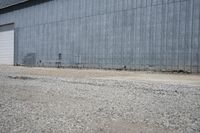 two cars parked in front of a large warehouse building with concrete wall and large door