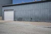 two cars parked in front of a large warehouse building with concrete wall and large door