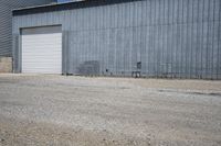 two cars parked in front of a large warehouse building with concrete wall and large door