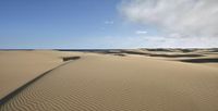 sand dunes and clouds in a wide open field with water in the distance and blue skies