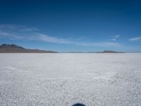 an empty desert with large rocks in the distance and a mountain in the distance across it