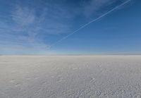 there is a plane flying above a flat plain with snow in it's air