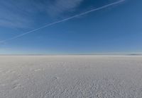 there is a plane flying above a flat plain with snow in it's air