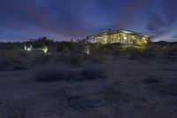 a house in the desert at night surrounded by trees and vegetation with its lights on