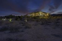 a house in the desert at night surrounded by trees and vegetation with its lights on