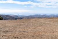 a barren mountain side, a lone person on the bench is overlooking a view of the distant mountains