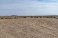 a brown grass field with trees on the far side and desert and hills in the distance