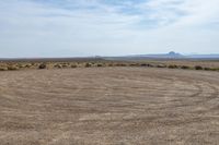 a brown grass field with trees on the far side and desert and hills in the distance