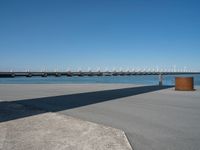 a concrete bench on the sidewalk near water with sailboats in distance behind it,