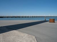 a concrete bench on the sidewalk near water with sailboats in distance behind it,