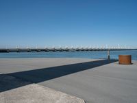 a concrete bench on the sidewalk near water with sailboats in distance behind it,