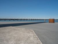 a concrete bench on the sidewalk near water with sailboats in distance behind it,