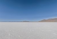 view across vast flat expanse to mountains with sparse sand flooring and sky in the distance