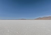 view across vast flat expanse to mountains with sparse sand flooring and sky in the distance