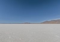 view across vast flat expanse to mountains with sparse sand flooring and sky in the distance