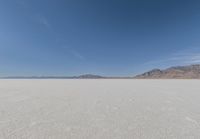 view across vast flat expanse to mountains with sparse sand flooring and sky in the distance