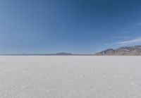 view across vast flat expanse to mountains with sparse sand flooring and sky in the distance