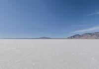 view across vast flat expanse to mountains with sparse sand flooring and sky in the distance