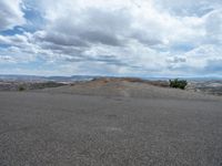 the person is riding their skateboard down a hill of empty sand as clouds and blue skies