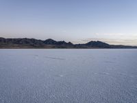 a lake with no water, in a mountainous plain at dusk with small mounds and mountains behind